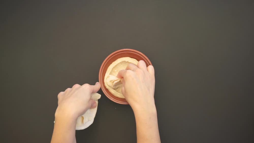 hands reach into a bowl of hummus from an aerial perspective